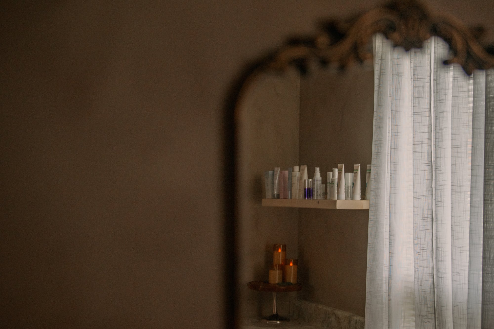 Treatment room corner with an arched mirror, sheer curtain, and shelf of skincare products