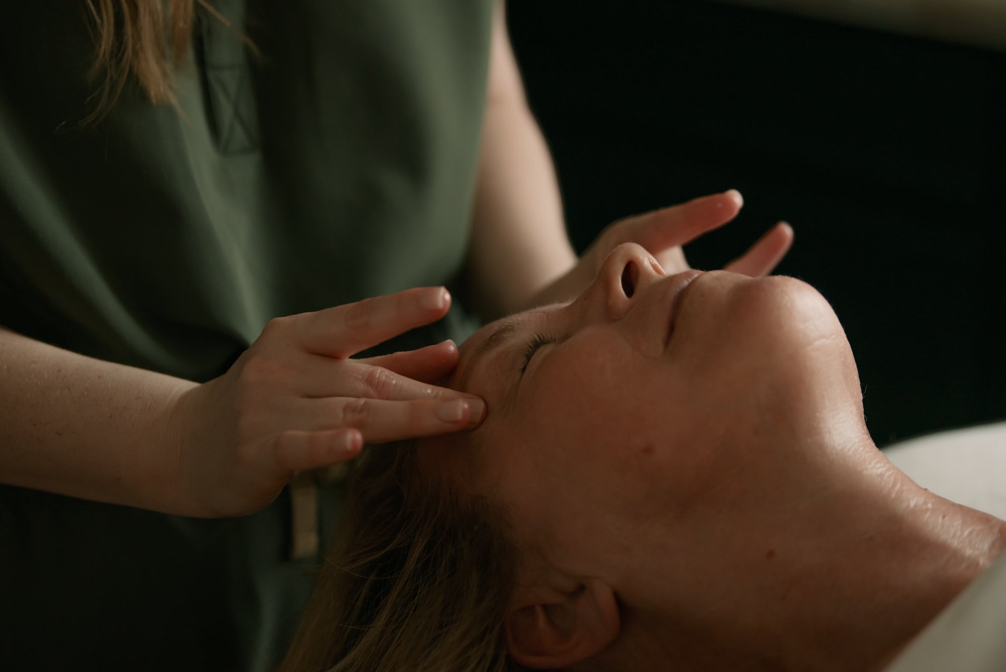 Esthetician performing a facial massage on a relaxed client in soft, low light