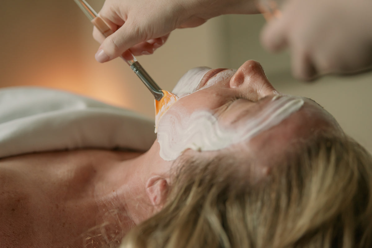 Gloved esthetician brushing chemical peel solution across a client's face