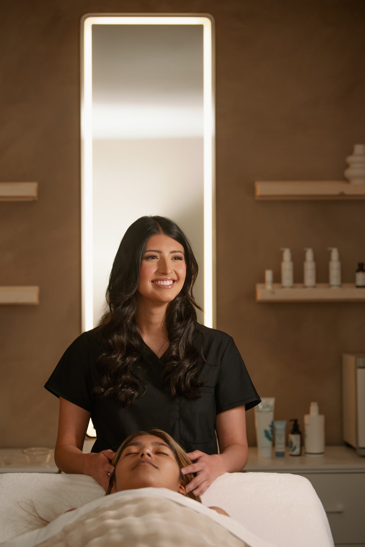 Autumn, esthetician at Esthetics With Me, smiling beside a client on the facial bed
