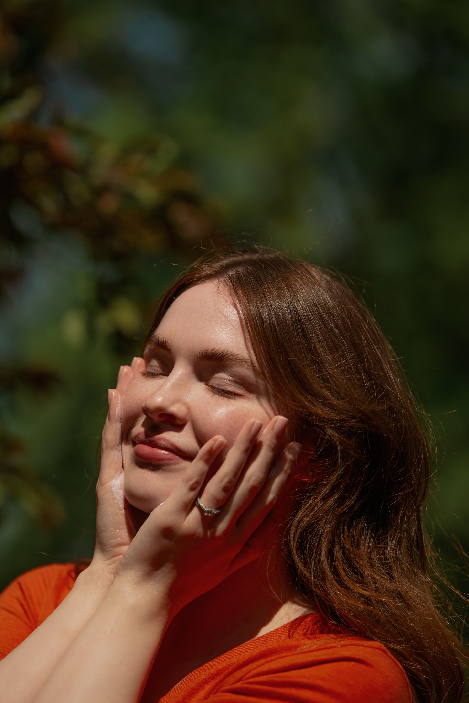 Client smiling outdoors with her hands framing her clear, healthy skin