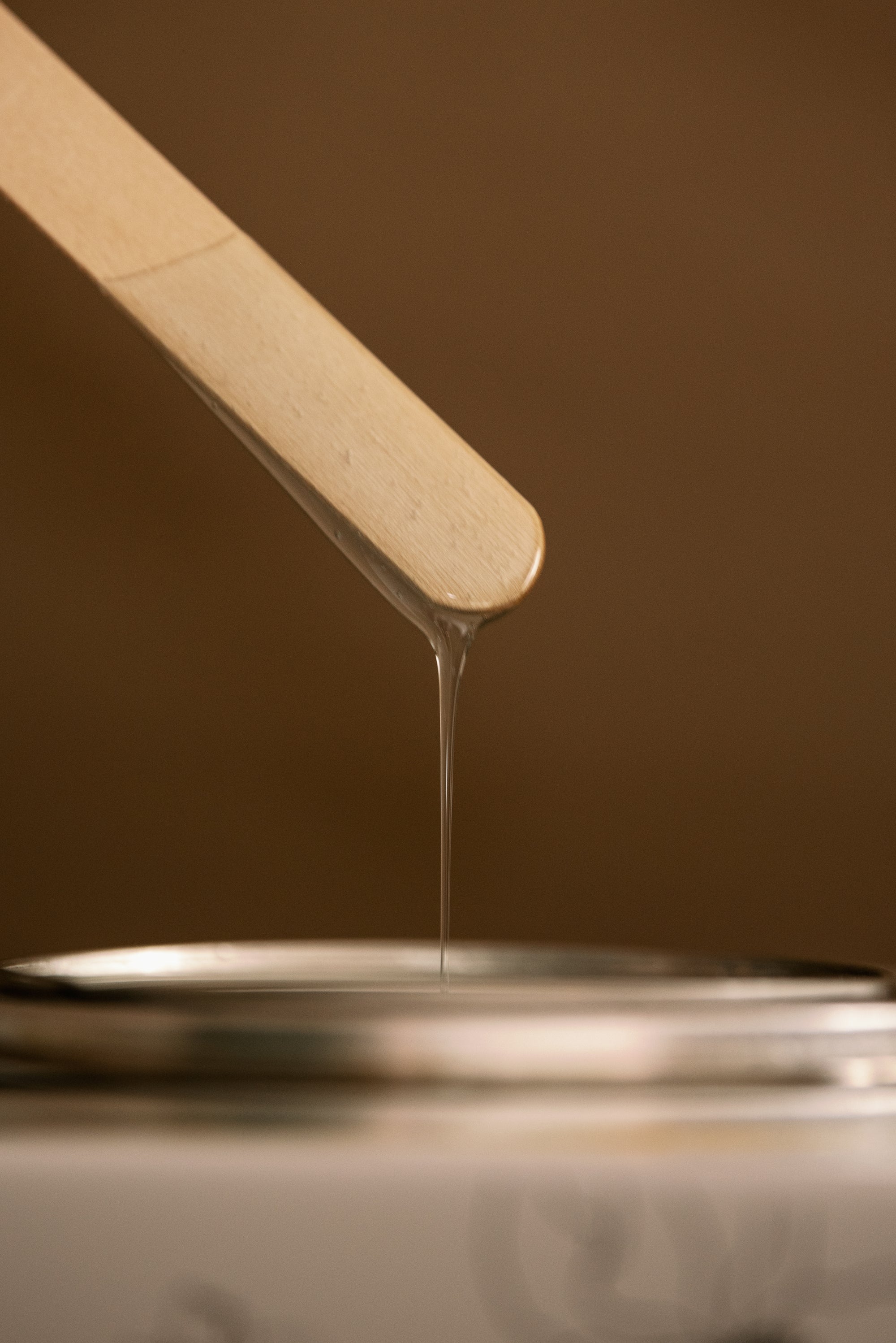 Close-up of warm wax dripping from a wooden applicator into the wax warmer