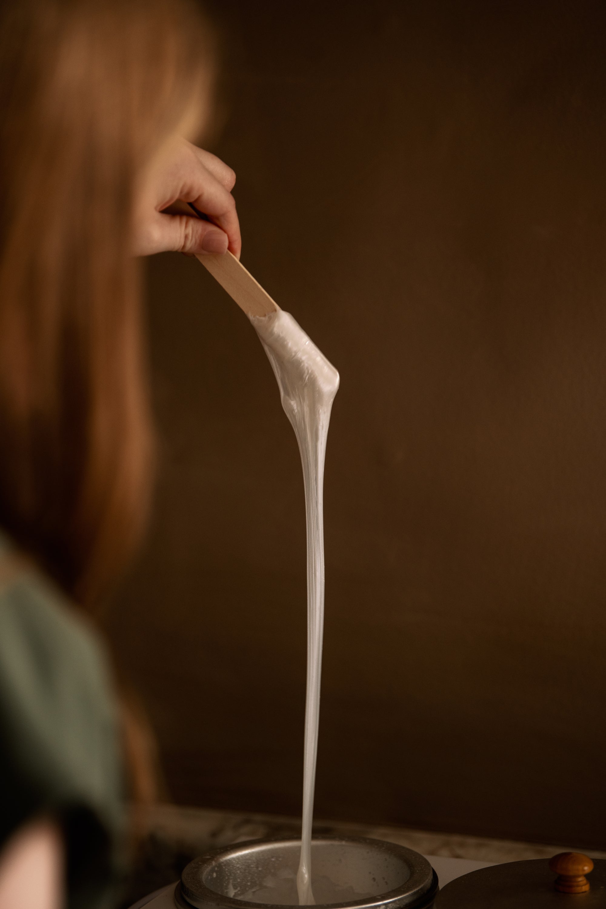 Warm wax stretching from a wooden applicator into the wax pot