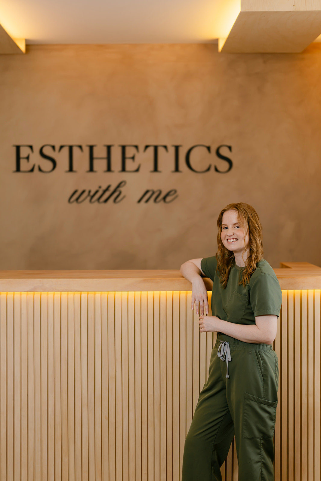 Esthetician at the front desk beneath the Esthetics With Me sign in McHenry, IL