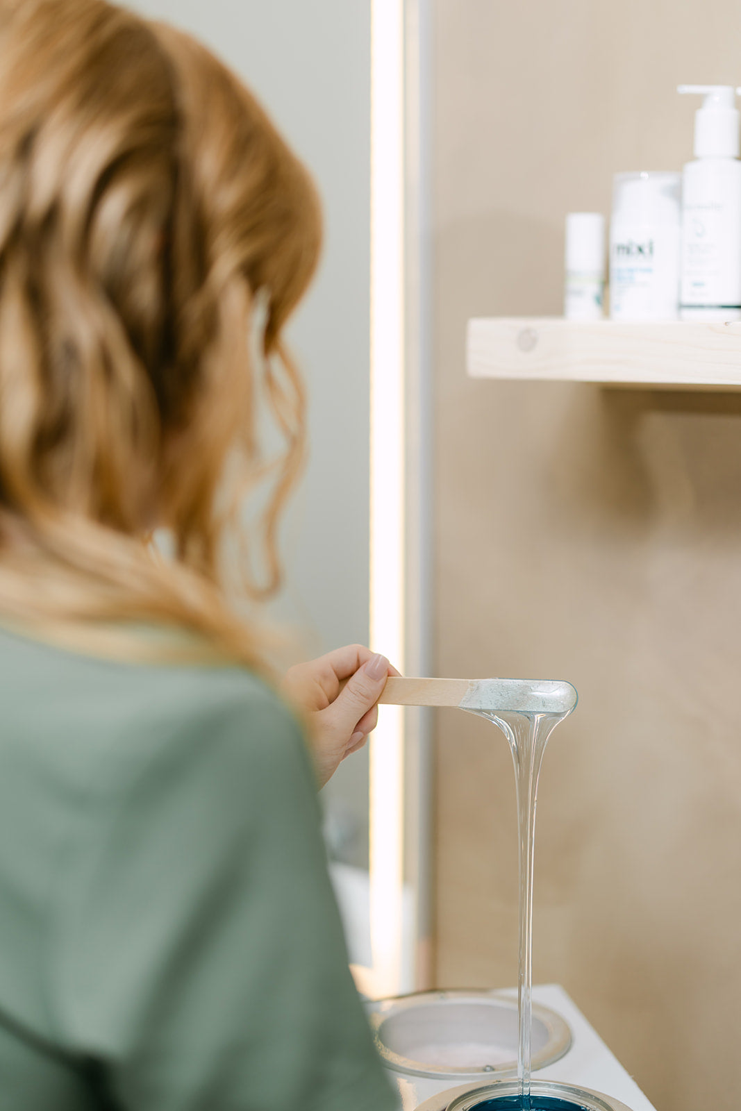 Esthetician pouring warm soft wax into a wax warmer before a waxing appointment