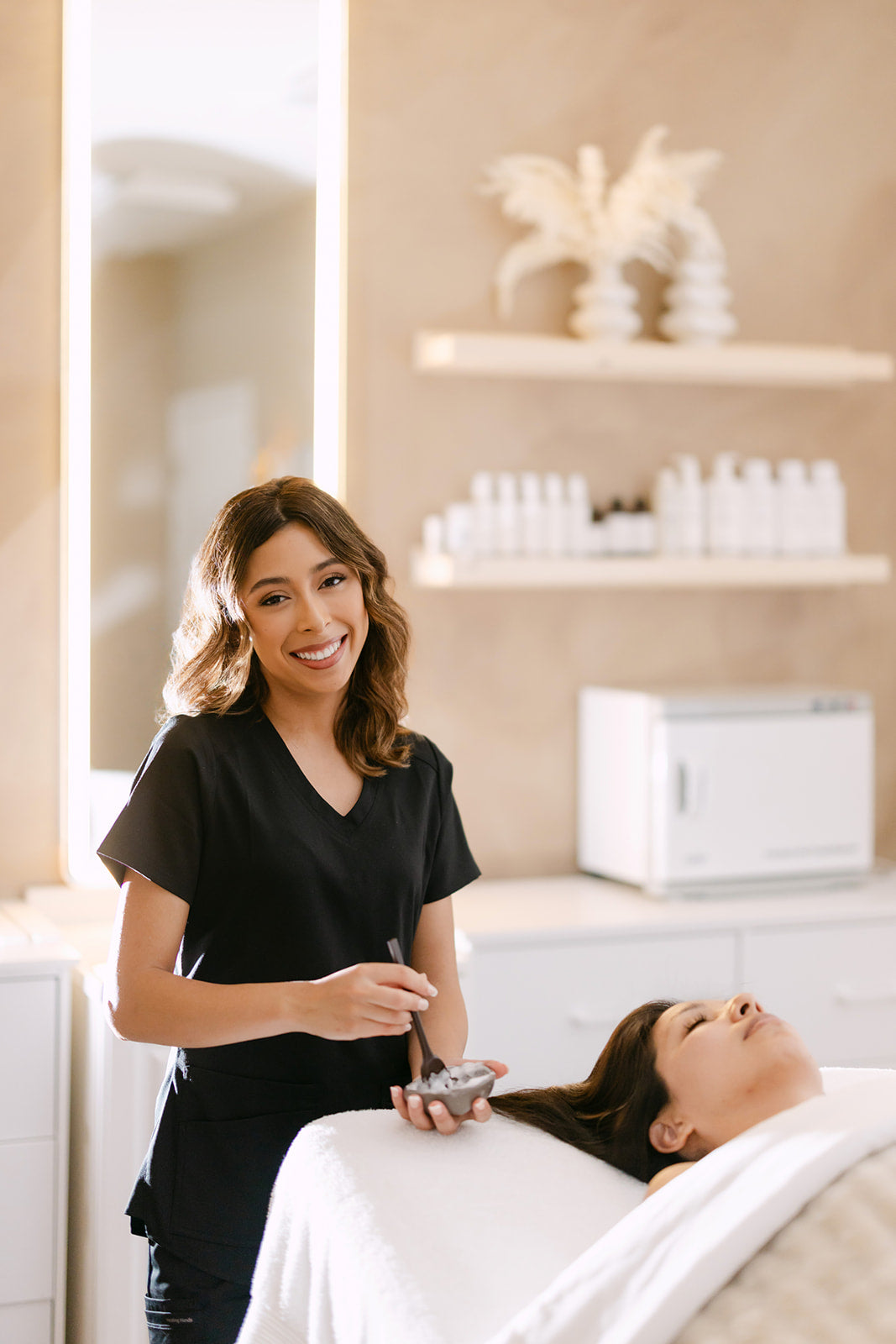Clarissa, esthetician at Esthetics With Me, treating a client's skin beside a lighted mirror