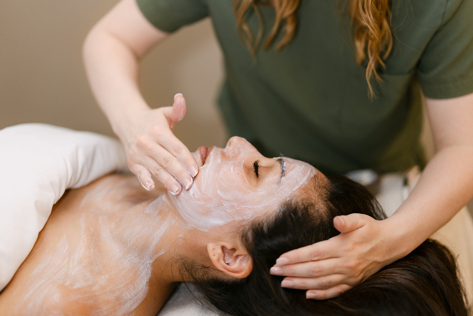 Esthetician massaging a creamy cleanser across a client's face during a facial