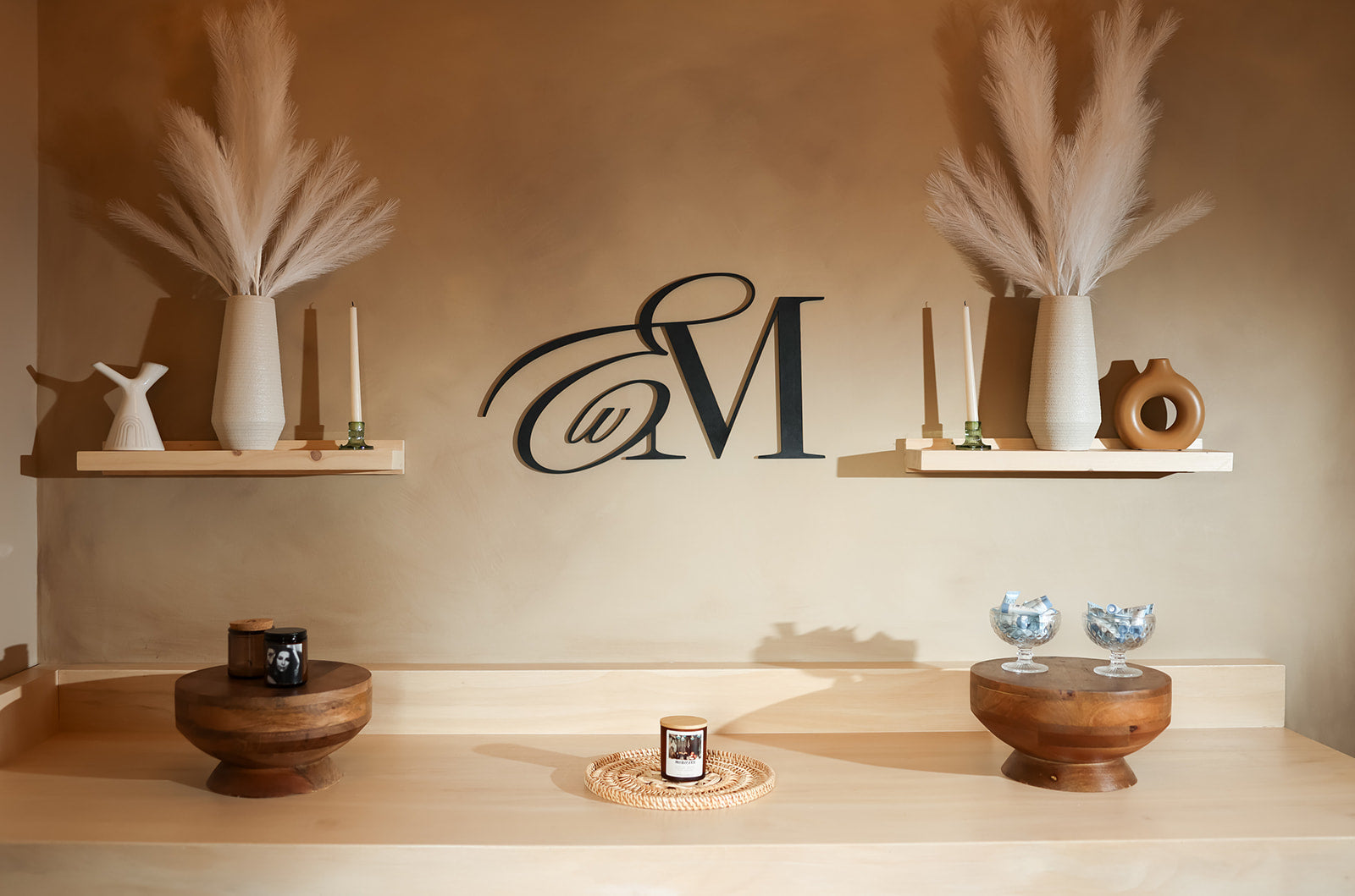 Esthetics With Me monogram on the studio feature wall above candles and dried pampas grass