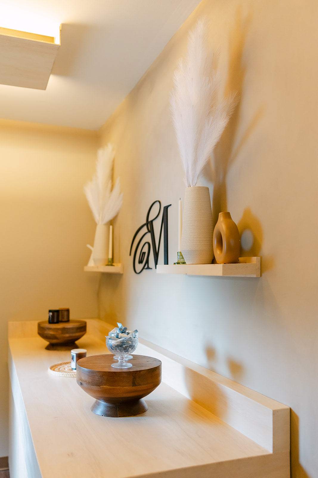 Esthetics With Me monogram on the studio feature wall above candles and dried pampas grass